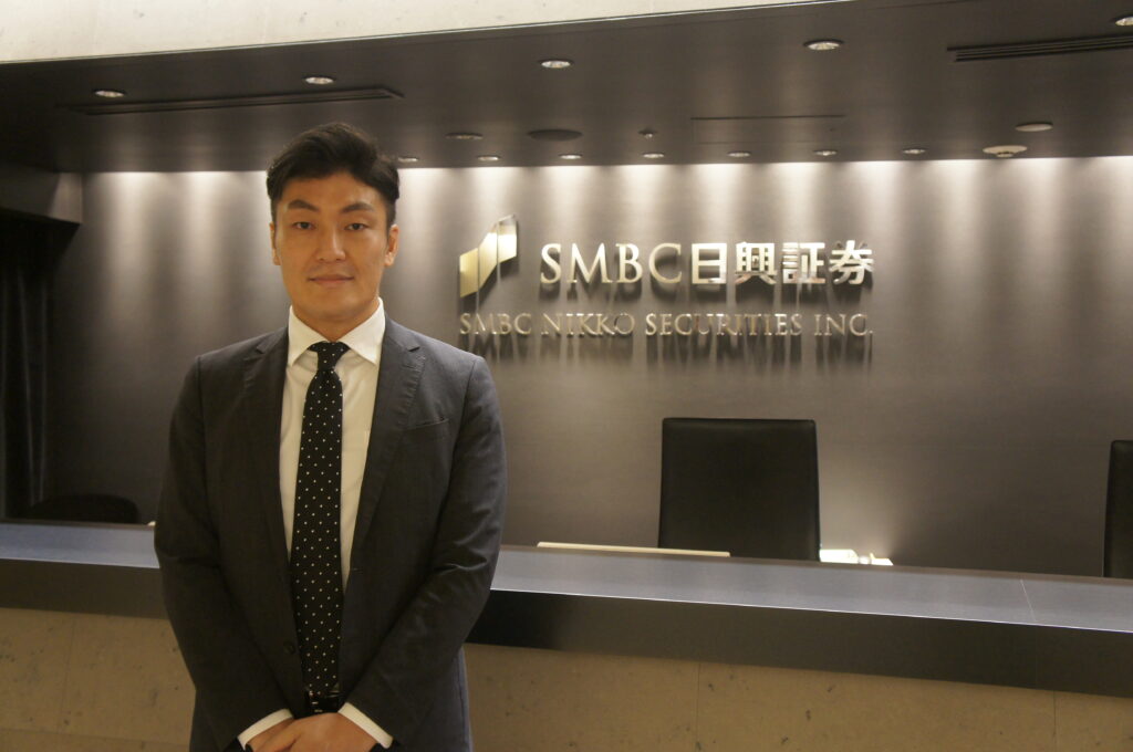 SMBC日興証券のロゴの前に立つ西澤さん