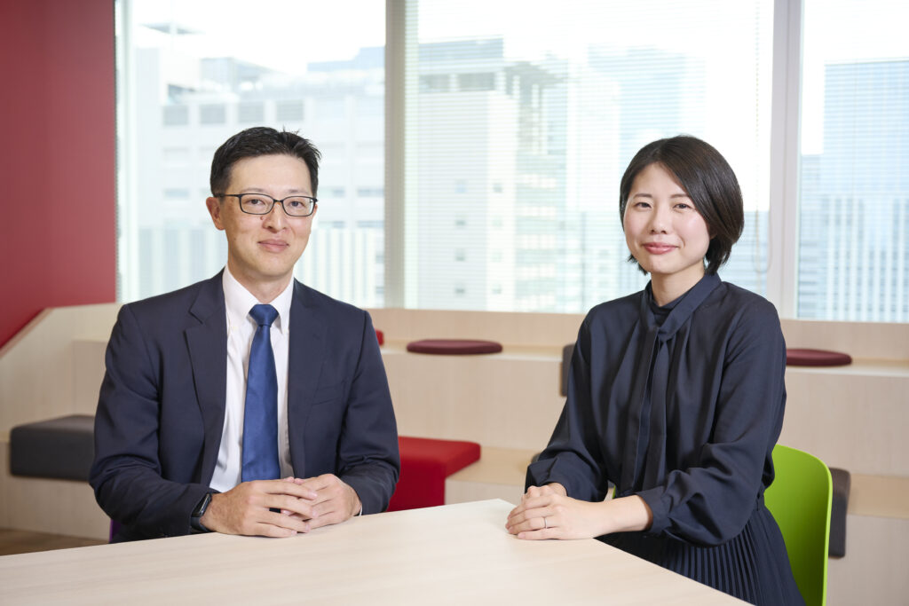 椅子に座ってテーブルの上で手を組み笑顔の秋葉さん左、牛尾さん右。